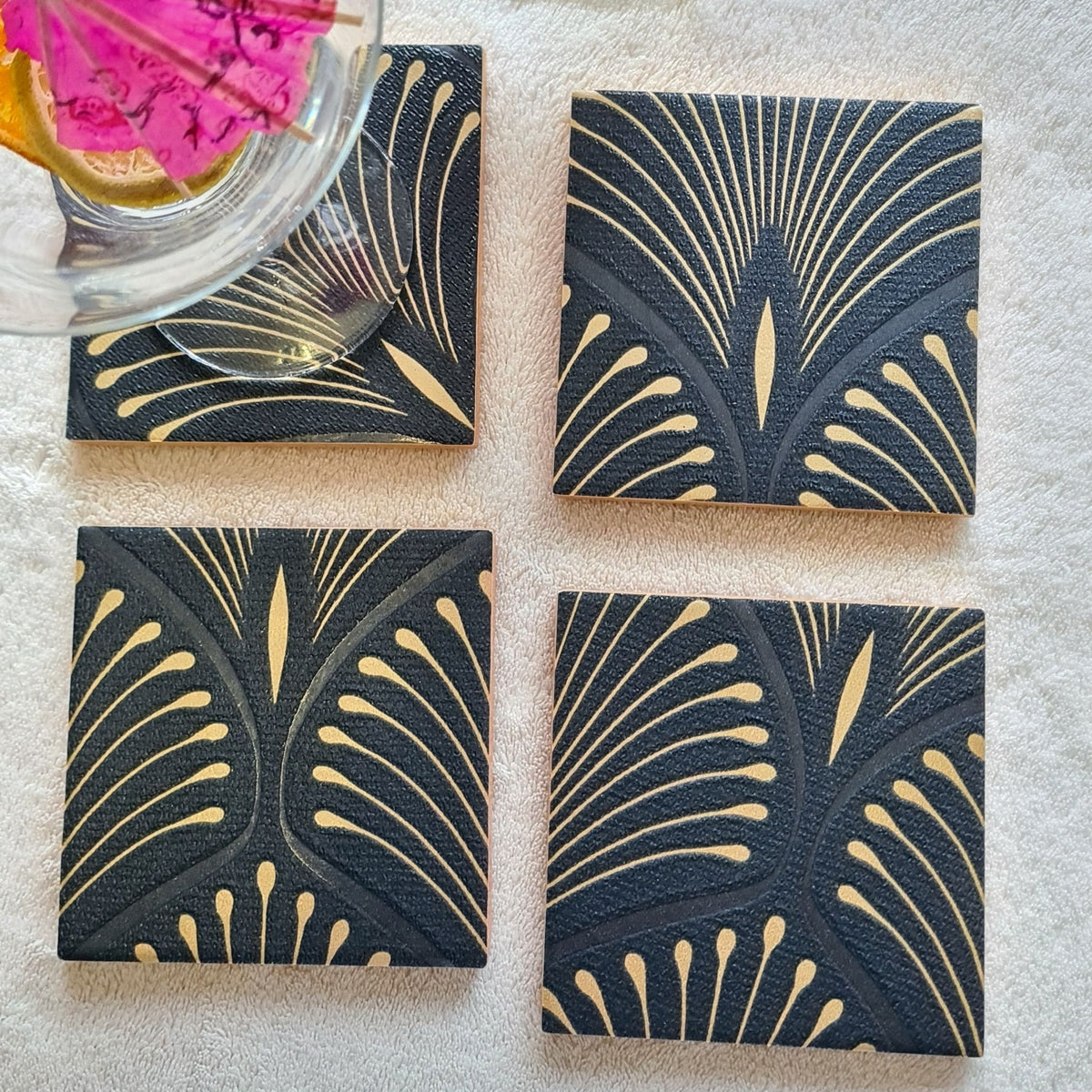 Handmade ceramic coasters featuring an elegant geometric Art Deco fan design in navy blue and bronze, styled with a cocktail.