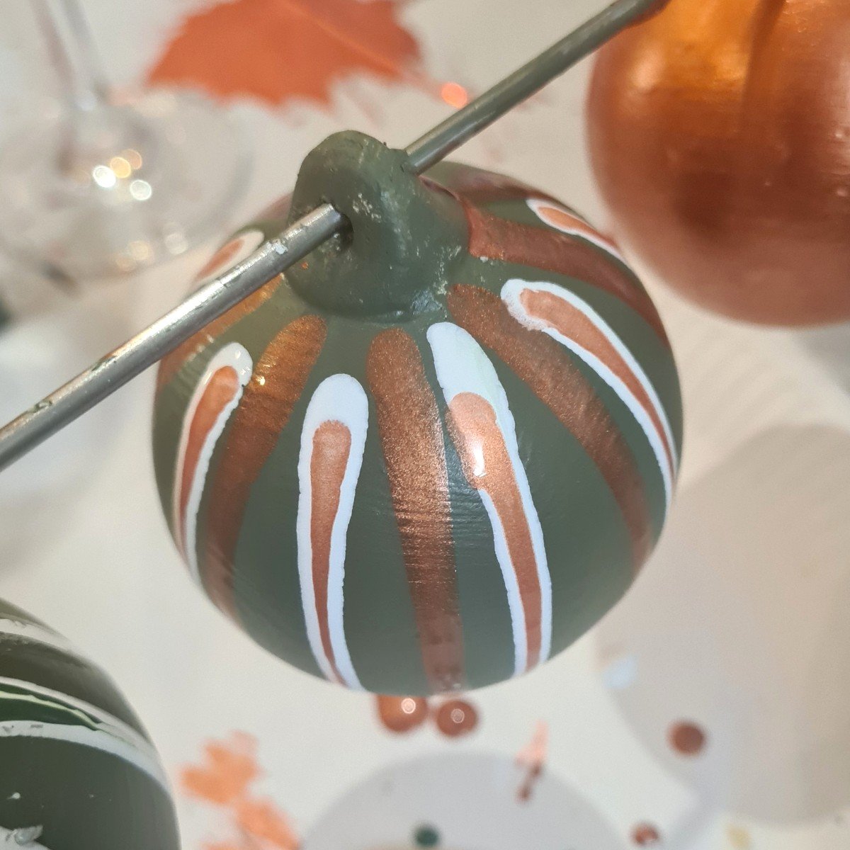 Hand-painted ceramic bauble, decorated with a dark green base, metallic copper-drizzles, and white painted accents.