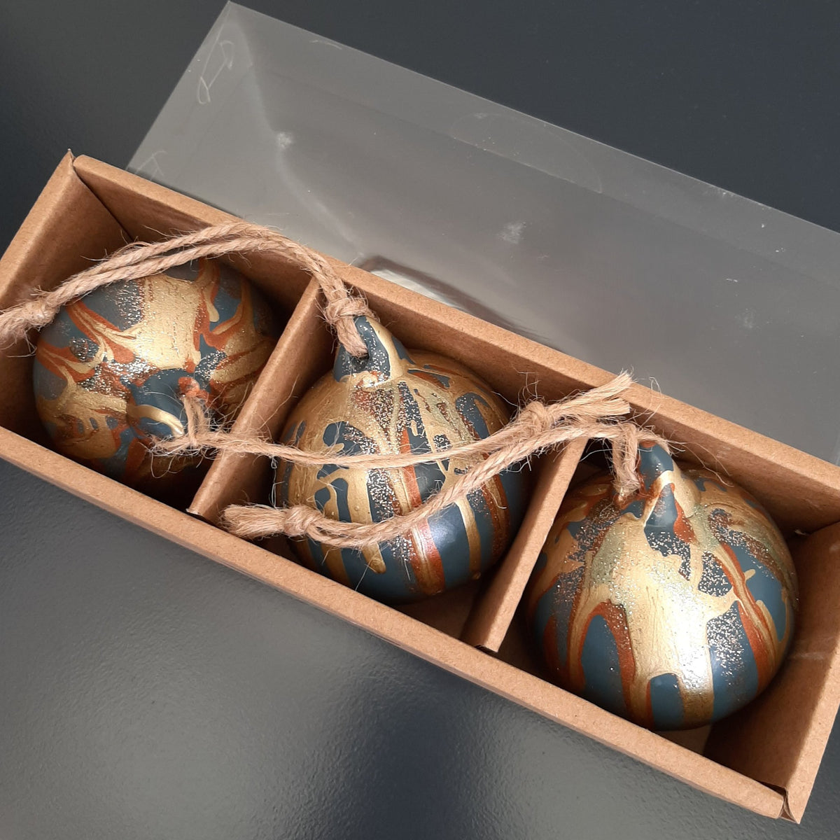 Three painted Christmas baubles in a storage gift box with twine, created at a Baubles and Bubbles party in Stotfold.