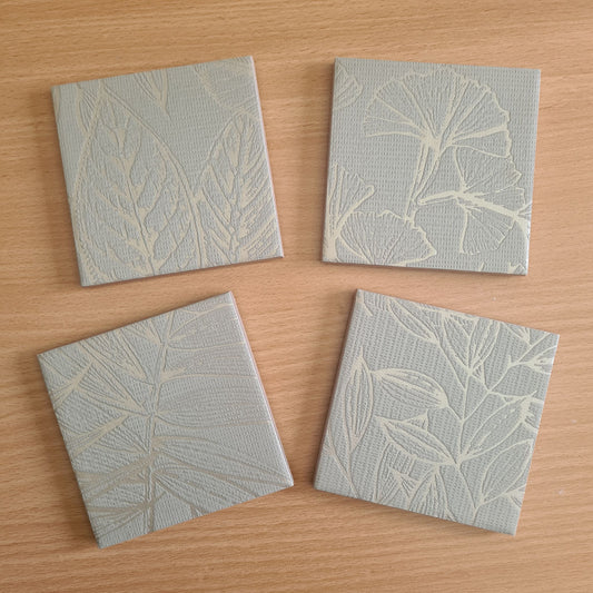 Limited-edition set of four handmade ceramic coasters with sage green ginkgo leaves and metallic Champagne details.