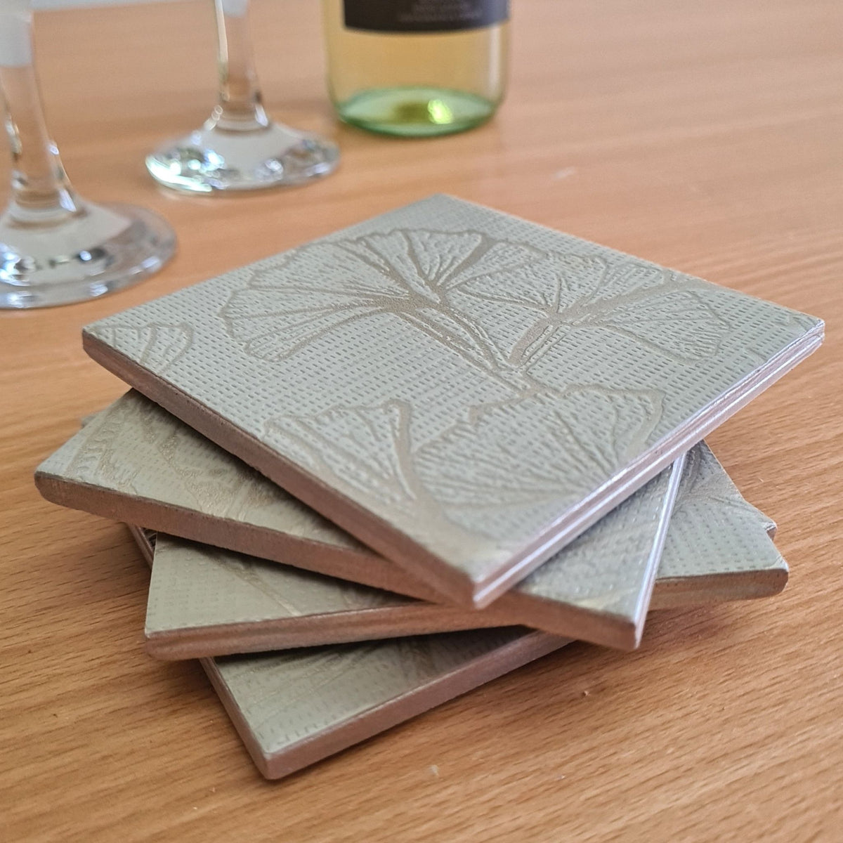 Close-up of metallic Champagne ginkgo leaves on a soft sage green handmade ceramic coaster.
