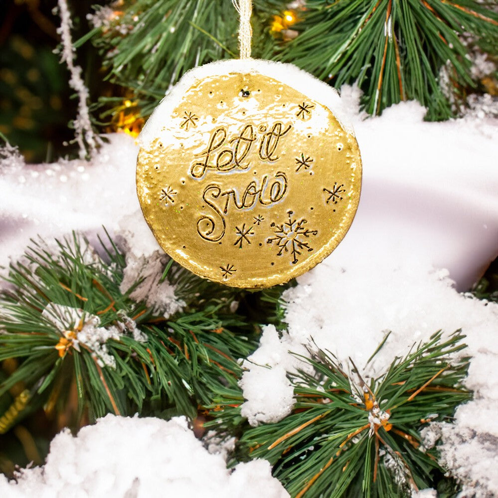 Handmade gold embossed Christmas decorations with Let It Snow hanging on a Christmas tree.