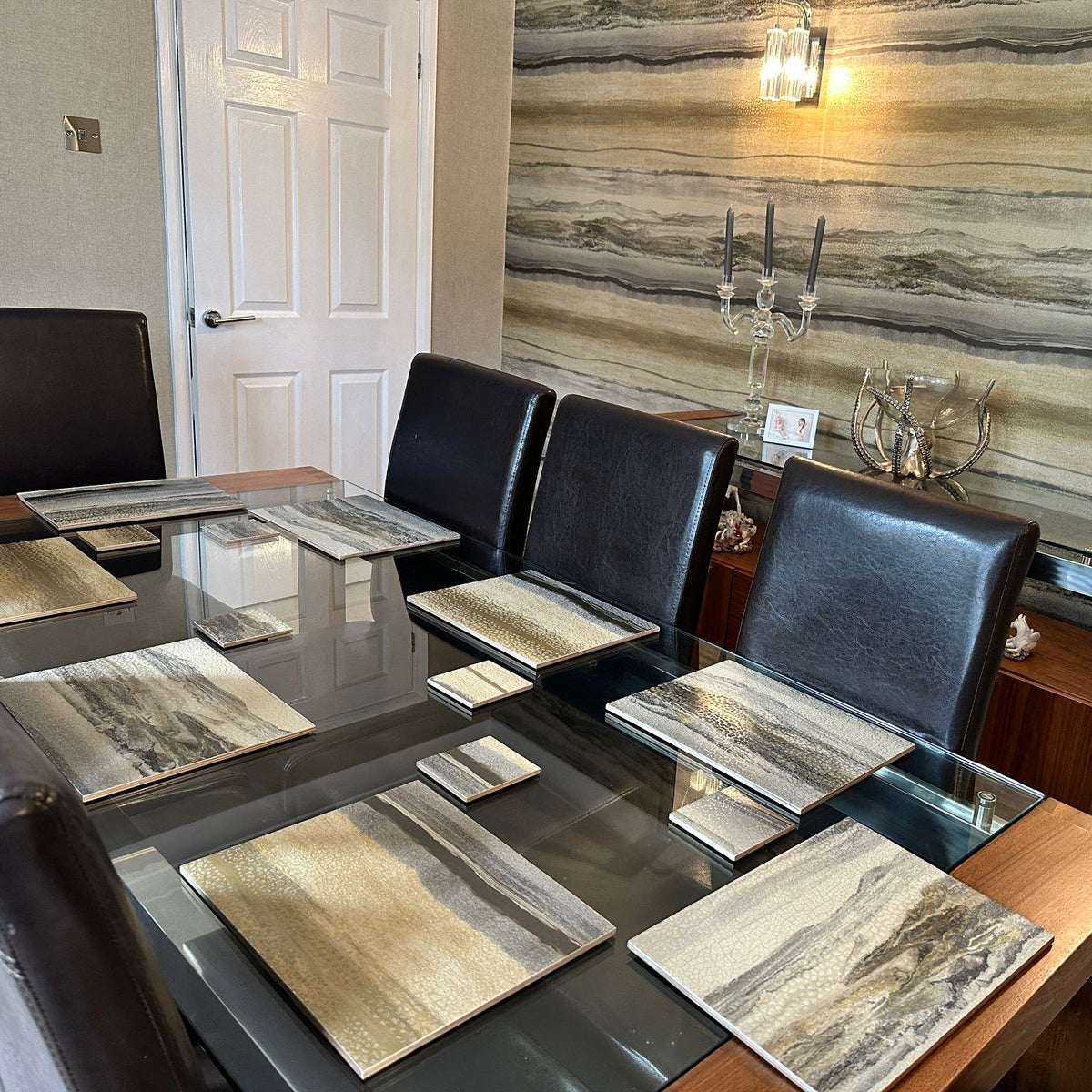 A dining table set with rectangular placemats and coasters which perfectly match the wallpaper, a textured, abstract stone-like pattern in neutral tones, created by The Furniture Bureau.