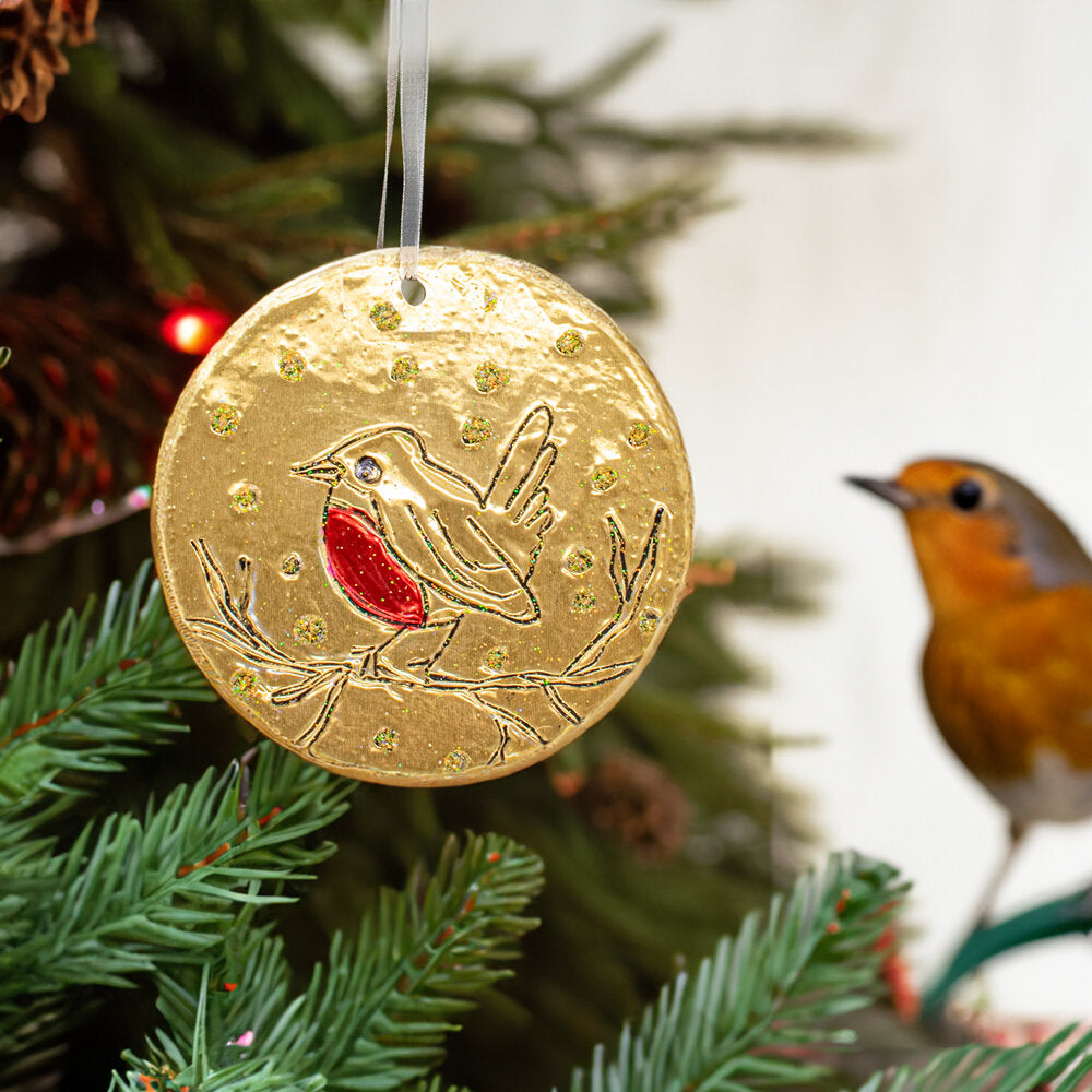 Handmade gold embossed Christmas decoration with robin hanging on a Christmas tree.