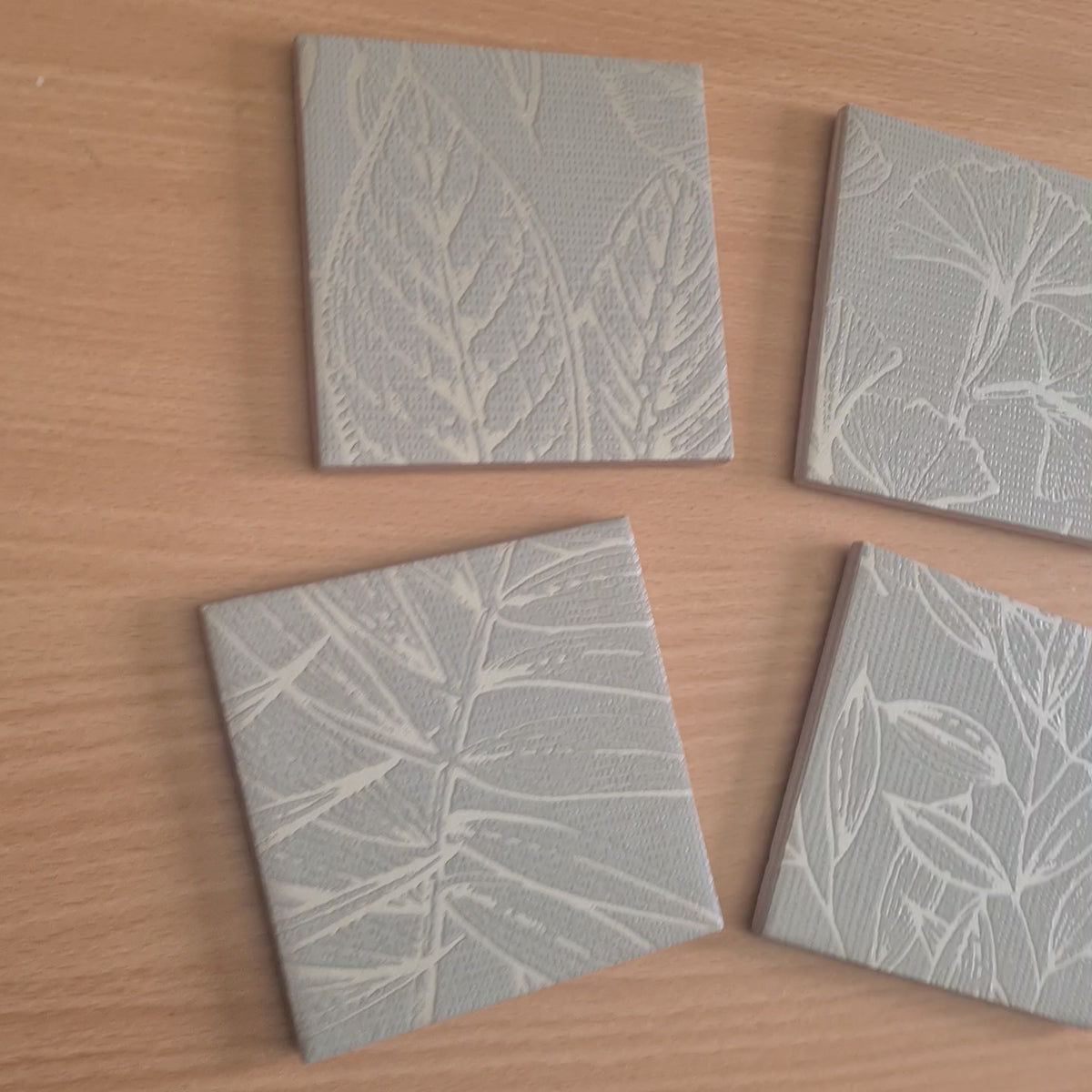 Limited-edition handmade ceramic coasters showing the sage green botanical design and metallic Champagne ginkgo leaf details.

