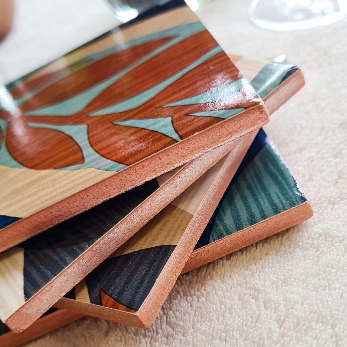 Stack of limited-edition set of four handmade Retro Leaf ceramic coasters in teal, burnt orange, blue, beige and cream with metallic copper edging.