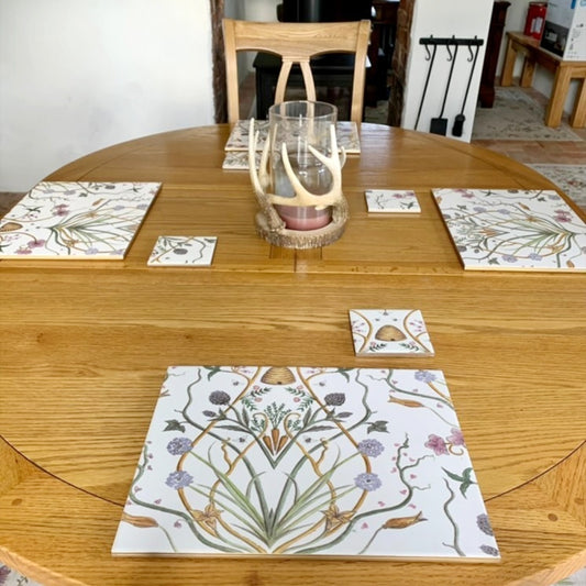 A set of handmade ceramic table place mats and coasters, created from Chateau Potagerie wallpaper, arranged on a round wooden dining table.