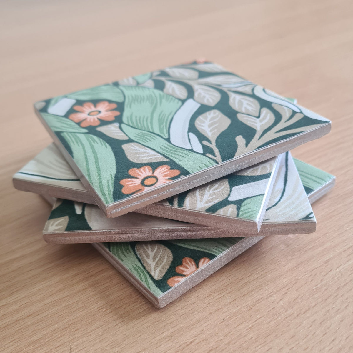 Close-up of champagne metallic edging on a stack of handmade William Morris Pimpernel ceramic coasters.