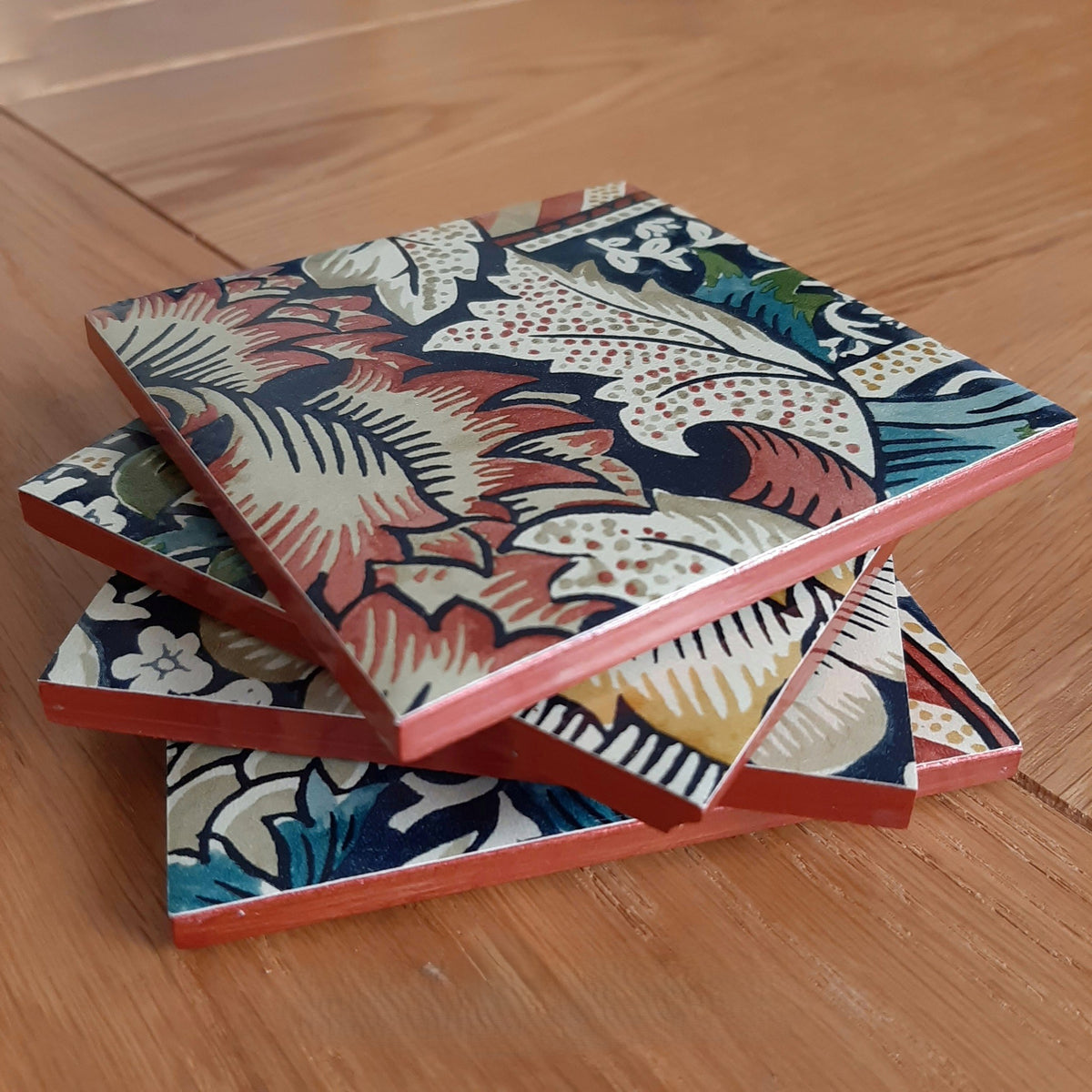 Stacked William Morris Wandle ceramic coasters showing their handcrafted rusty red metallic edging.